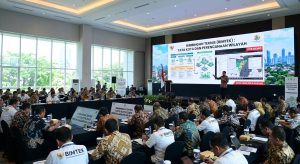 Suasana acara Bimbingan Teknis (Bimtek) Tata Kota dan Perencanaan Wilayah di dalam sebuah aula besar. Puluhan peserta berpakaian batik dan kemeja putih tampak duduk menyimak materi dari narasumber di panggung. Layar LED besar di depan menampilkan peta spasial dan diagram infografis perkotaan dengan judul "BIMBINGAN TEKNIS (BIMTEK): TATA KOTA DAN PERENCANAAN WILAYAH".