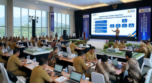 Foto suasana Bimbingan Teknis (Bimtek) Manajemen Konstruksi & Infrastruktur di dalam aula besar. Puluhan peserta berseragam dinas PNS dan batik duduk menghadap laptop di meja panjang, memperhatikan narasumber di panggung. Layar LED besar di depan menampilkan materi infografis alur manajemen proyek dengan latar belakang biru, lengkap dengan maket jembatan dan bangunan di beberapa sudut ruangan.