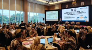 "Sebuah foto candid dari dalam aula konferensi besar di Indonesia, menangkap suasana dinamis dari lokakarya 'Bimtek Pemerintahan dan Administrasi'. Sekitar 150 peserta pemerintah Indonesia (PNS) dalam kemeja Batik atau seragam resmi, pria dan wanita, duduk di meja bundar, aktif terlibat. Mereka mendengarkan presenter, seorang pria berjas dan kacamata, di panggung dengan layar proyeksi besar yang menampilkan judul acara dalam teks bahasa Indonesia yang menonjol: 'BIMBINGAN TEKNIS (BIMTEK): PEMERINTAHAN DAN ADMINISTRASI YANG BAIK DAN BERSIH'. Di bawahnya terdapat poin-poin dan ikon yang terkait dengan birokrasi, seperti 'REFORMASI BIROKRASI' dan 'PELAYANAN PUBLIK'. Sebuah spanduk tergantung di atas panggung dengan lambang negara Indonesia (Garuda Pancasila) dan logo kementerian penyelenggara, mungkin Kemendagri, dengan tulisan 'PUSDIKLAT' dan 'BIMTEK 2026'. Peserta di latar depan memiliki folder, buku catatan, dan laptop terbuka di meja mereka. Beberapa berdiskusi dalam kelompok kecil, yang lain mencatat atau memotret layar dengan ponsel pintar mereka. Pelayan bergerak diam-diam, menawarkan minuman. Aula ini memiliki jendela besar di satu sisi yang menghadap ke pepohonan dan sore yang berawan di sebuah kota di Indonesia. Lampu sorot menerangi panggung, dan cahaya alami dari jendela menciptakan suasana yang cerah dan fokus. Komposisinya dinamis, menangkap kedalaman ruangan dan keterlibatan orang-orang."