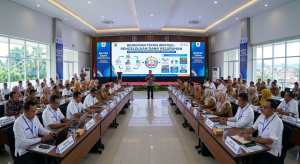 Foto suasana Bimbingan Teknis (Bimtek) Pengelolaan Dana Kelurahan di dalam aula. Puluhan peserta berseragam dinas PNS dan kemeja putih duduk rapi berhadapan dalam formasi meja berbentuk U. Di ujung ruangan, seorang narasumber berdiri di depan layar LED besar berlatar biru-putih yang menampilkan infografis bertuliskan "BIMBINGAN TEKNIS (BIMTEK): PENGELOLAAN DANA KELURAHAN - MEWUJUDKAN TRANSPARANSI DAN AKUNTABILITAS".